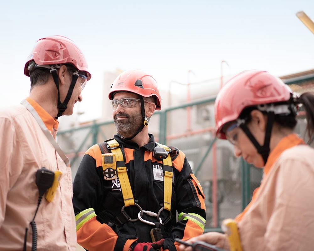 Tres trabajadores con cascos rojos hablando entre ellos