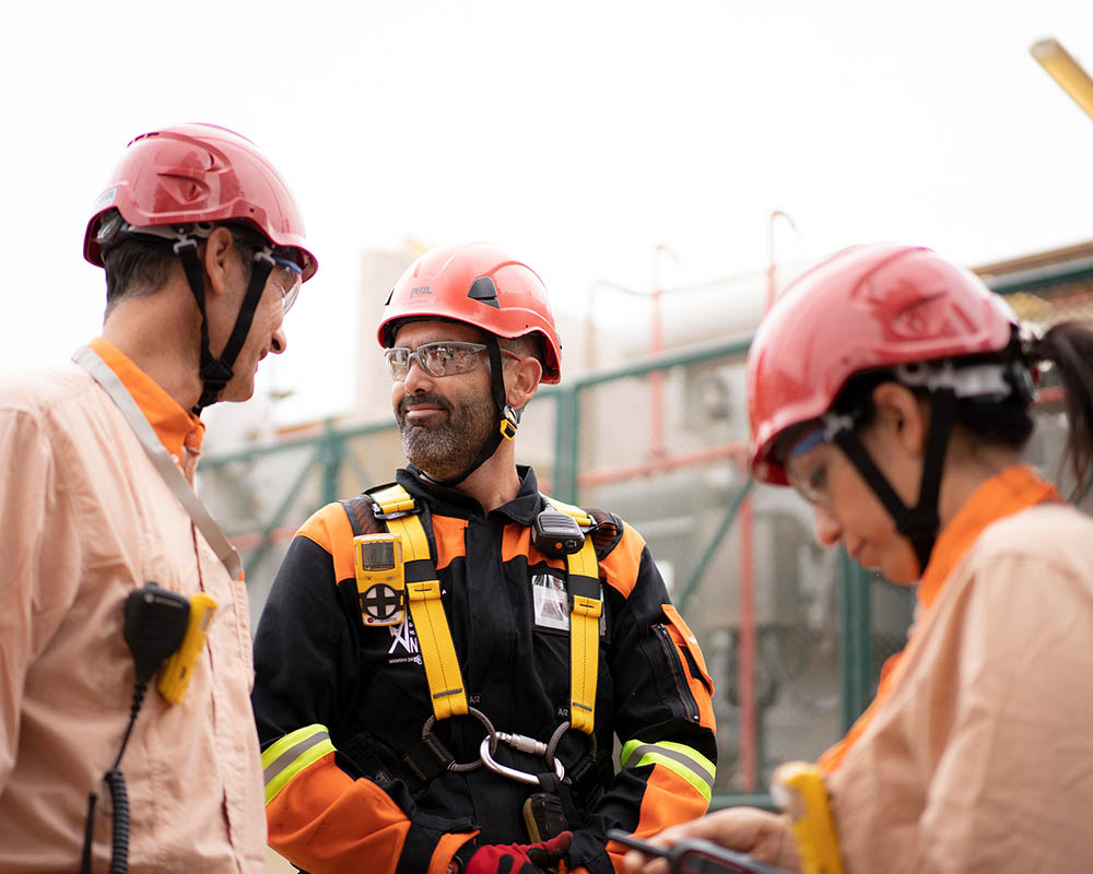 Three workers in red helmets talk to each other