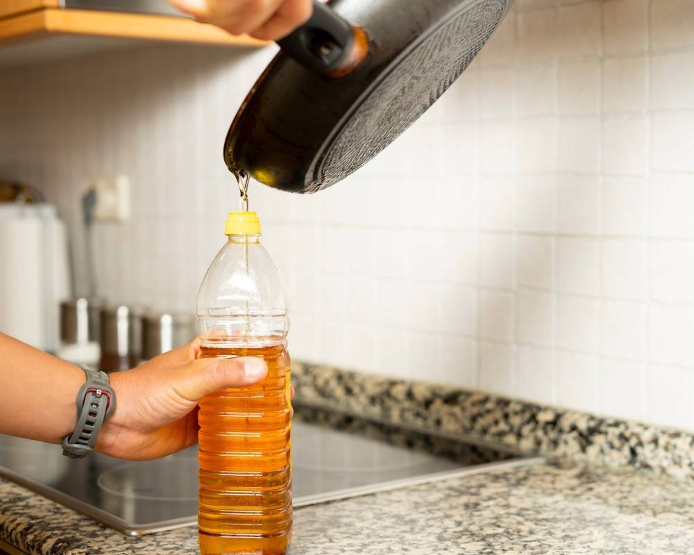 Recogiendo el aceite de cocina usado desde una sartén a una botella de plástico