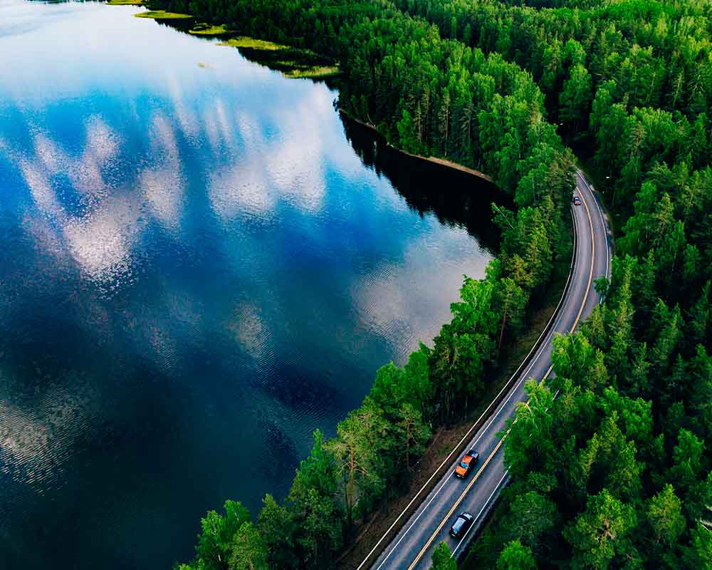 Cars driving on a road that surrounds a lake