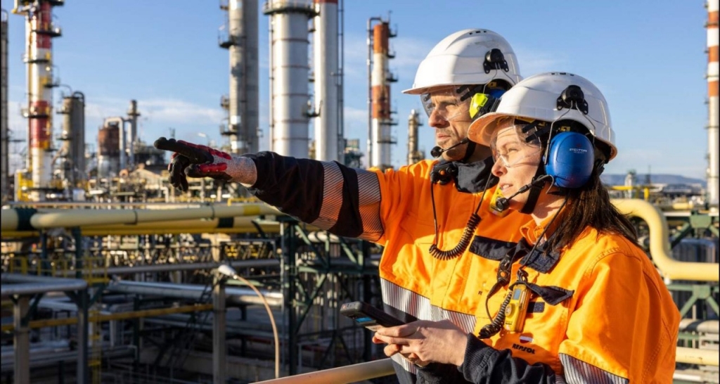 Two workers in an industrial complex wearing safety helmets