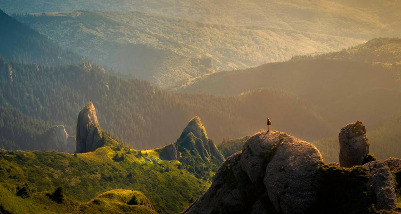 Paisaje de montañas con luz del sol y una persona en la punta de una montaña