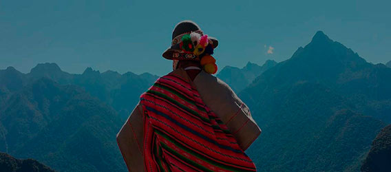 Vista de espaldas de una persona ataviada con ropajes autóctonos mirando un paisaje montañoso al atardecer 